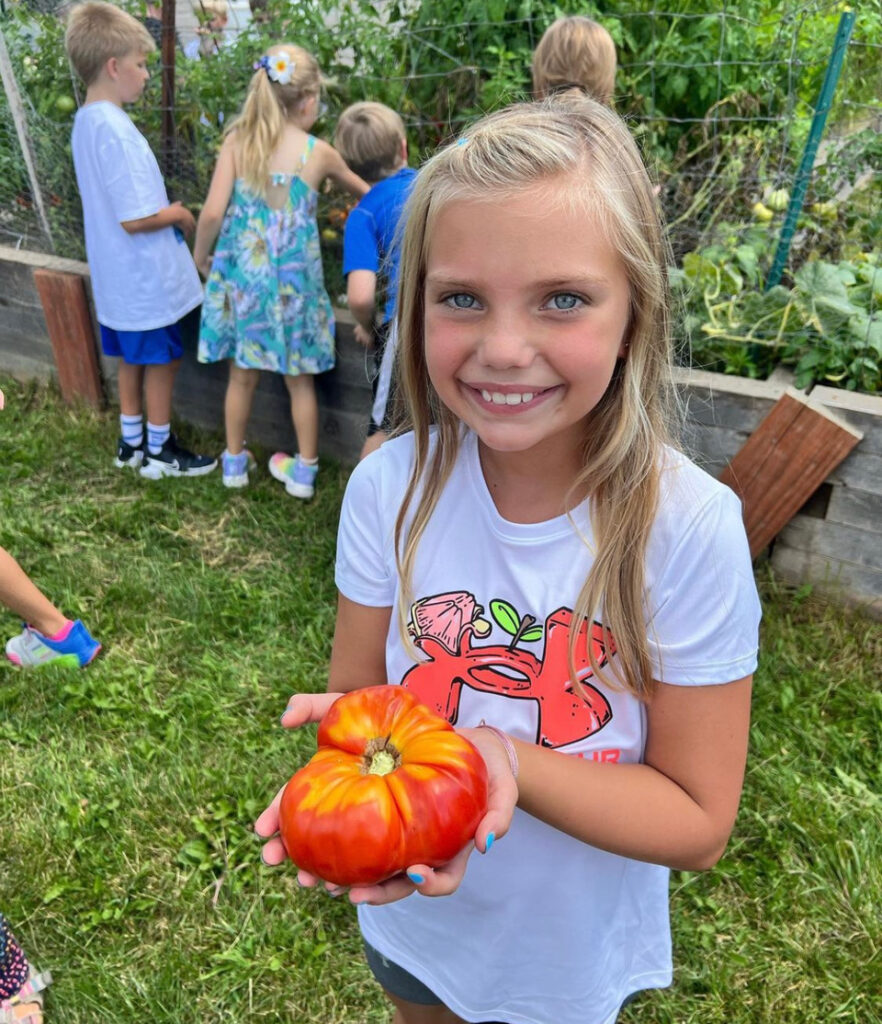 Carrie Lee student holding tomato from a raised garden bed.